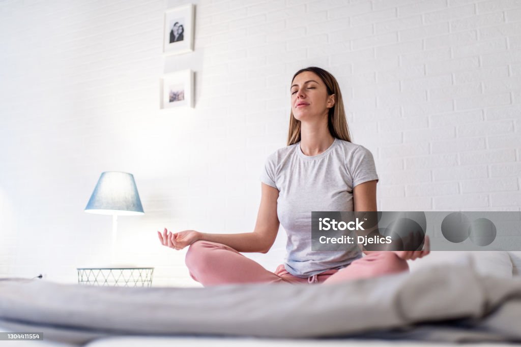 Woman meditating in the bedroom. Young woman meditating in the bedroom in the morning. Routine Stock Photo