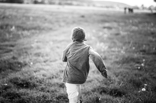 Only one boy with blonde hair is running in the meadow. He is wearing a baseball cap and a protective mask. Krakow in Poland. Black and white