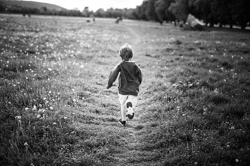 Only one boy with blonde hair is running in the meadow. He is wearing a baseball cap and a protective mask. Krakow in Poland. Black and white