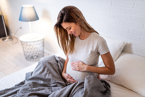 Photo of happy mid adult pregnant woman relaxing at home and looking at her future baby.