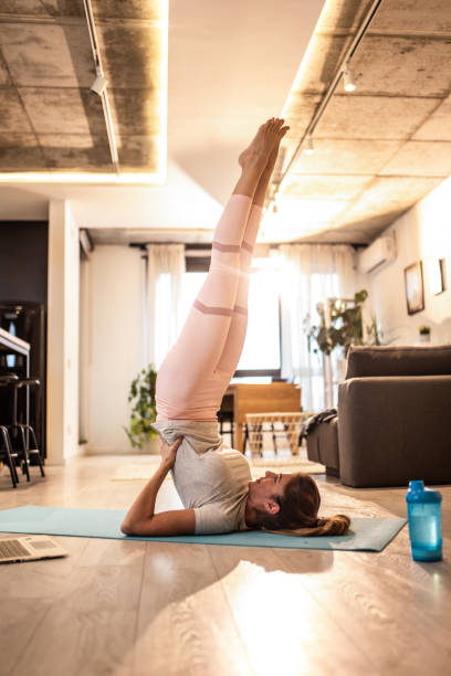 Mid adult sportswoman doing supported shoulder stand while working out at home Athletic woman practicing Yoga in supported shoulder stand pose in the living room. shoulder stand stock pictures, royalty-free photos & images
