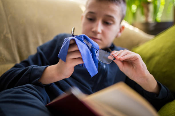 Cute boy wearing glasses reading book on couch, homeschooling concept