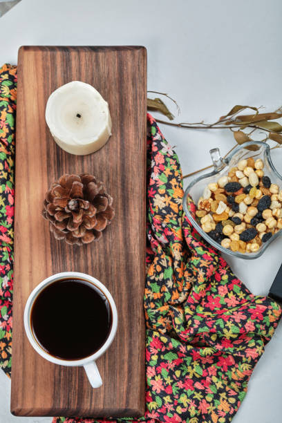 A cup of coffee with candle, forest cone, nuts on the wooden board