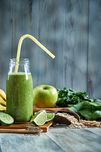 green smoothie in glass, spirulina powder, vegetables and fruits on white ceramic tile background. healthy, raw, vegan diet concept.