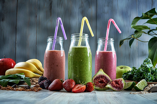 Healthy food: Set of three banana blackberry, strawberry and green detox smoothies in bottles with straws on a rustic table in a rustic kitchen.