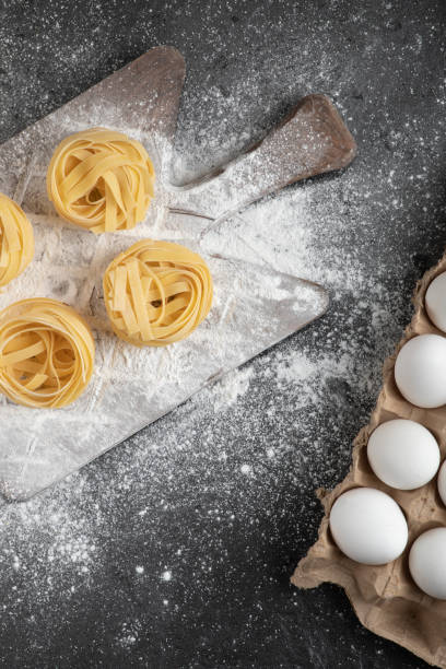 istock Raw fresh tagliatelle nests with flour on wooden board and eggs 1304436509
