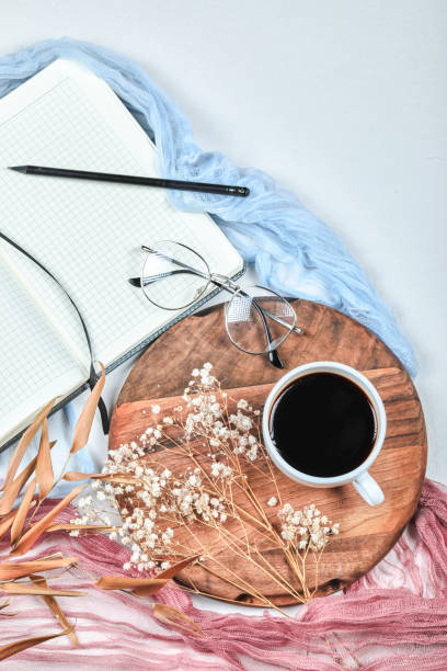istock Open notebook, glasses, a cup of tea and dried plants on white desk 1304436530