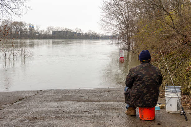 Man Fishing in Cumberland River February 27, 2021 - Nashville, Tennessee, U.S.: A man fishes in the Cumberland river from the boat ramp in Shelby park. The water is high and almost covers the stop sign. tennessee road sign stock pictures, royalty-free photos & images