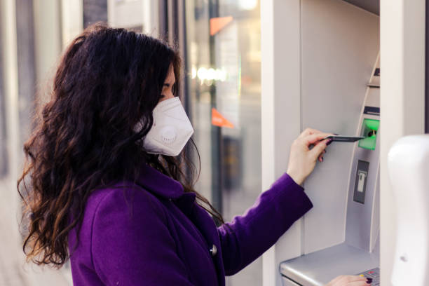 istock Adult woman is using a ATM while wearing mask. 1304437767