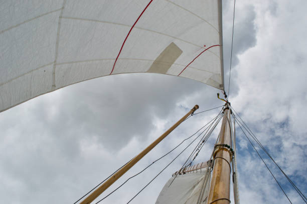 Looking up the mast of a gaff rigged sailing yacht Looking up the mast of a gaff rigged sailing yacht: white sails, wooden mast and gaff, rope shrouds, halyards and sheets, and blue cloudy sunny sky gaff sails stock pictures, royalty-free photos & images