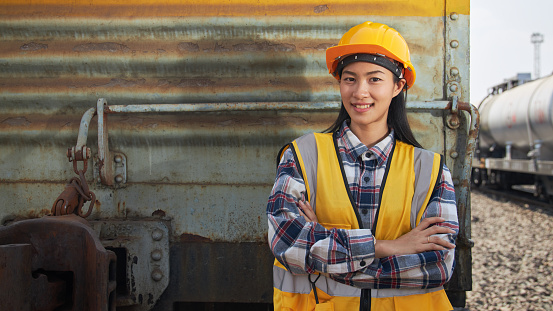 Portrait of female engineer standing and arms crossed outdoors with petroleum tanker train and a freight train. The petroleum transportation industry by a rail system.
