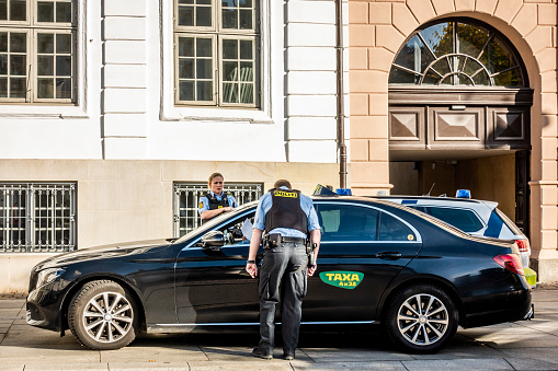 Copenhagen, Denmark - Oct 19, 2018: Male police officer stopped a taxi to interrogate driver while a female officer watches on the other side. Both wearing bulletproof vests. At Sankt Annae Place.