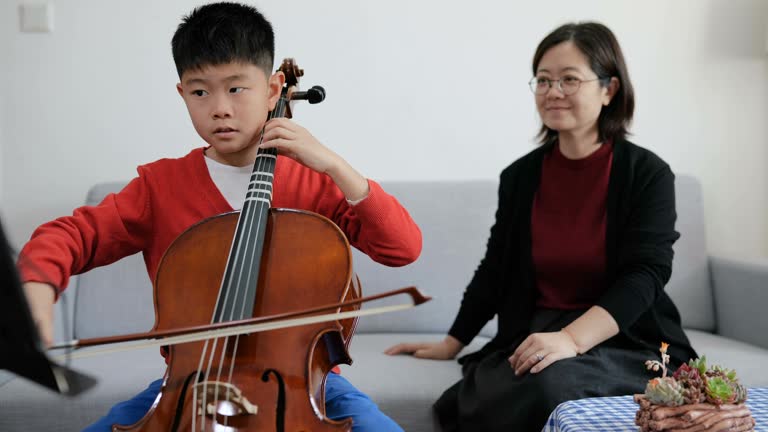 Panning view of young boy practicing cello with teacher at home