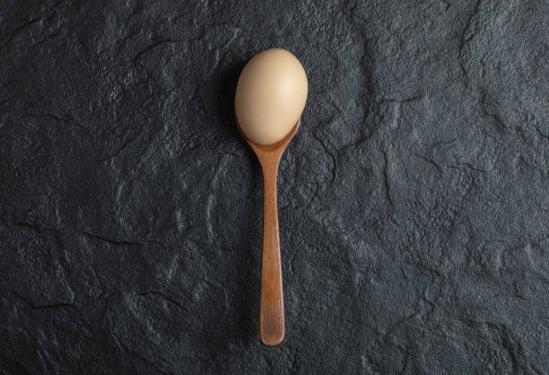 istock Wooden spoon of organic raw egg on black background 1304464155