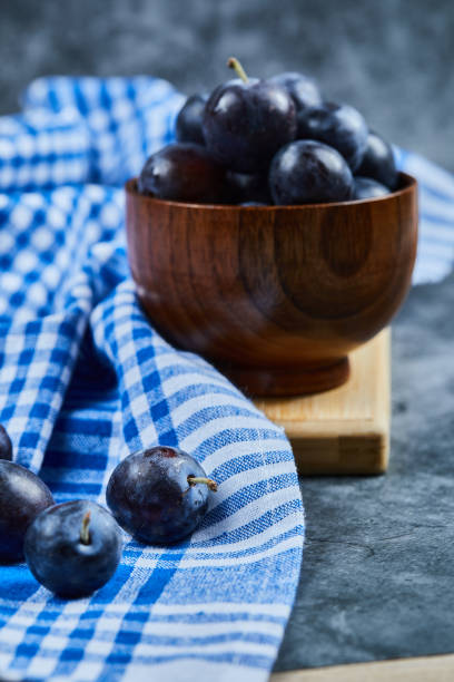Garden plums in a bowl on a marble background with tablecloth