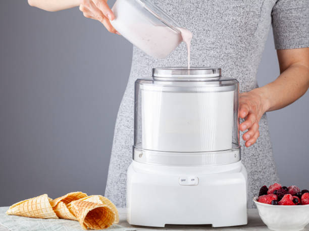 A caucasian woman is pouring homemade all natural ice cream mixture into an ice cream maker machine stock photo