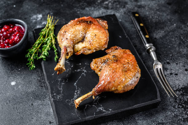 istock Roasted duck leg confit with cranberrie sauce. Black background. top view 1304483523