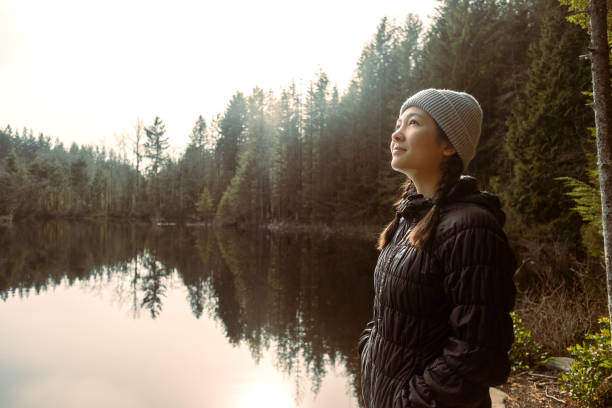 multi-ethnic young woman in quiet contemplation at edge of lake - nature forest clothing smiling imagens e fotografias de stock