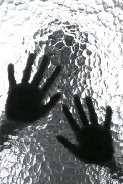 Photo of The silhouette of the person and its hand behind the door with the textured glass