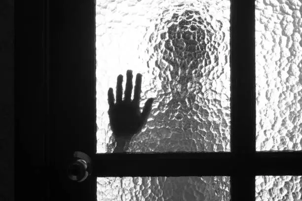 Photo of person standing over the door and its hand on the glass near the handle