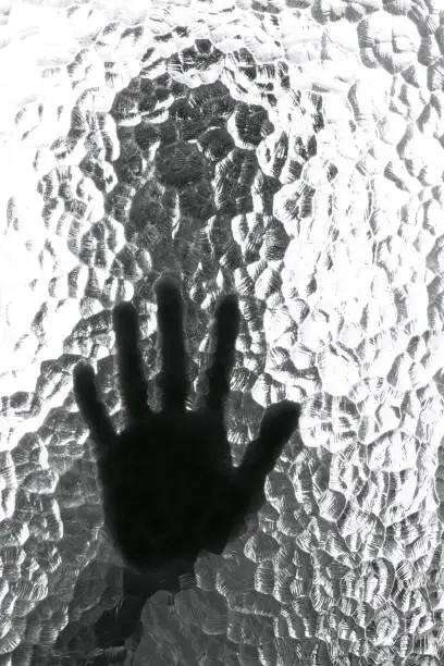 Photo of The silhouette of the person and its hand behind the door with the textured glass