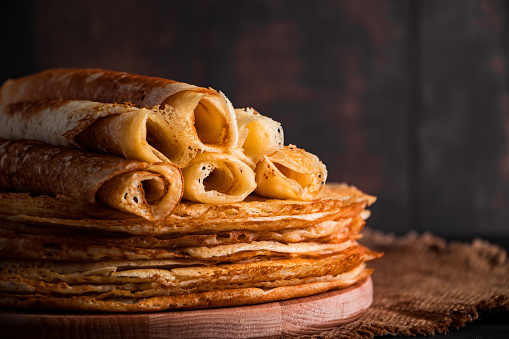 Traditional Russian food - thin pancakes. A stack of crepes on a dark brown wooden background. Rustic style.