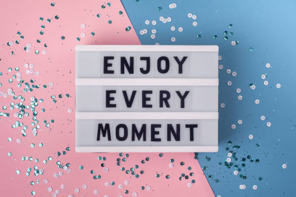 istock Enjoy every moment - text on display lightbox on blue and pink background. 1304487006