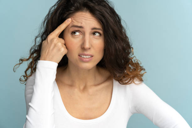 Scowling woman in shock of her acne, squeezing pimple on face, suffers from facial skin problems Close up of scowling woman in shock of her acne, squeezing pimple on face, suffers from facial skin problems, isolated on studio color blue background. Ugly infection of blackhead. wrinkled forehead stock pictures, royalty-free photos & images