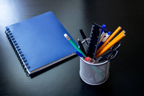 istock Stand with office supplies and blue notebook on black wooden table 1304487843