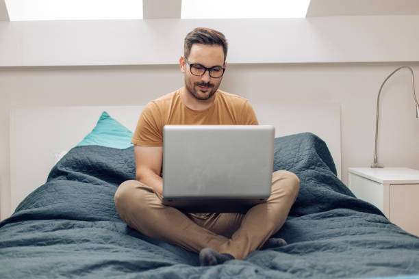 istock Young man sitting in his bed and working online 1304488071