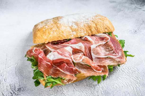 istock Prosciutto parma ham sandwich on ciabatta bread with arugula. White background. Top view 1304488166
