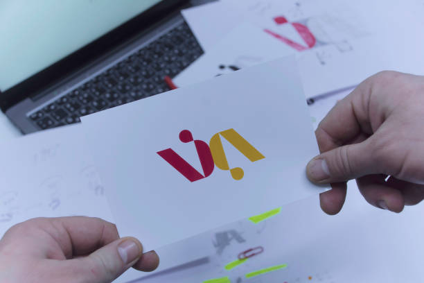 istock Creative workplace of a Graphic Designer. A man in the office is developing a logo on the table against the background of printed sketches and a laptop. 1304491841