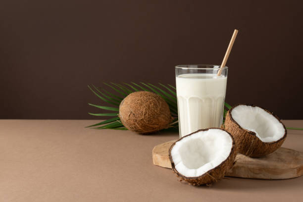 Coconut vegan milk with halves of nuts over brown background. A glass of coconut vegan milk with halves of nuts over brown background. coconut milk photos stock pictures, royalty-free photos & images