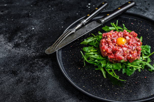 istock Beef tartare with arugula and quail egg. Black background. Top view. Copy space 1304494473