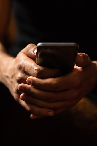 Person using smartphone. Close up of a smartphone in male hands in a cozy warm home environment