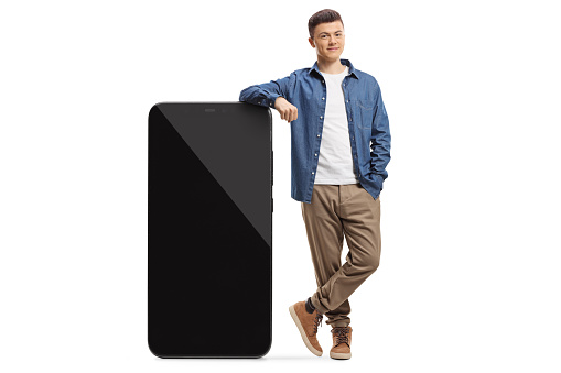 Full length portrait of a casual guy leaning on a big smartphone
