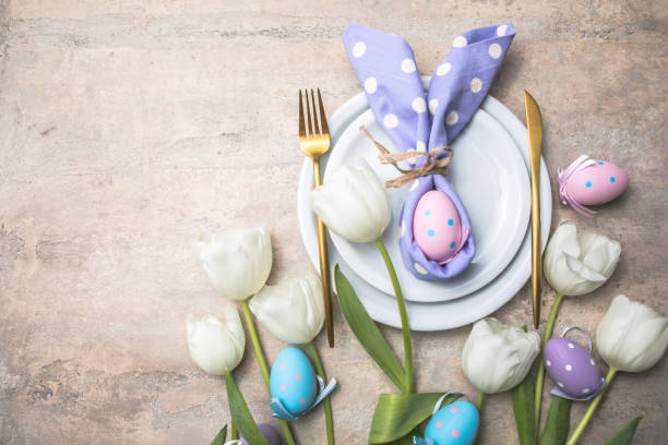 istock Easter holiday table setting with bunny  from egg on white plate and tulips flowers.  Gray concrete table, top view with copy space for text. Happy Easter background 1304497952
