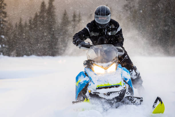 Homem se divertindo correndo com um snowmobile através da neve pó ao pôr do sol - foto de acervo