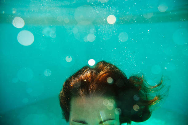 Horizontal view of unrecognizable woman diving into deep water. Blue blurred background and summer lifestyle. Underwater holidays in swimming pool concept. drowning photos stock pictures, royalty-free photos & images