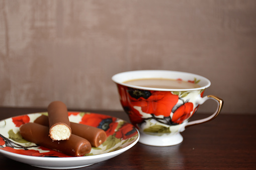 Coffee service with red poppies. Vintage cup of coffee with cream and a saucer with chocolate sweets.