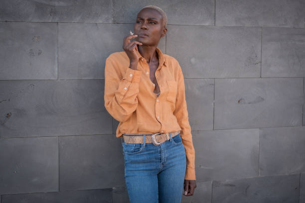 black adult woman smokes leaning against a gray wall outdoor focus on the face stock photo
