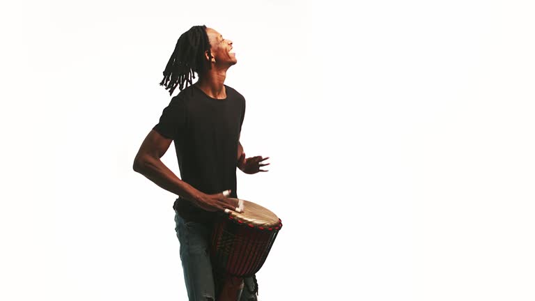 Black smile man plays the African drum with his hands in the studio. Happy musician dances and plays drum