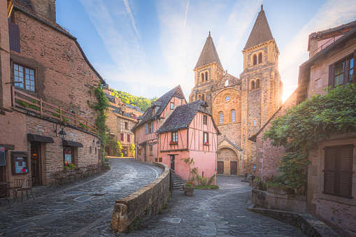 The quaint and charming town centre of the  medieval French village Conques, Aveyron and Abbey Church of Sainte-Foy at sunset or sunrise in Occitanie, France.