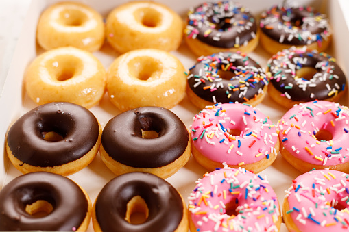 donuts with chocolate frosted, pink glazed and sprinkles in paper box, closeup