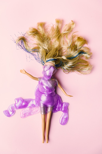 Layout of blondie doll laying on a pink background cover with purple shiny mass. After party minimal concept.