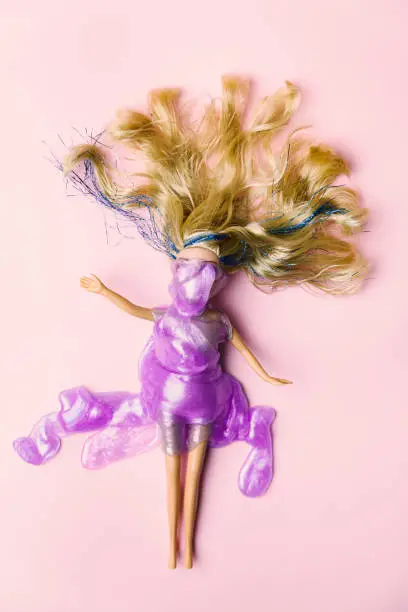 Photo of Layout of blondie doll laying on a pink background cover with purple shiny mass. After party minimal concept.