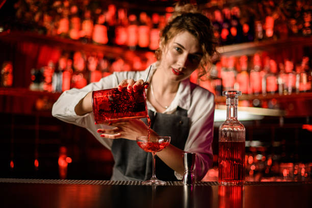pretty woman bartender pouring bright cocktail into glass on bar counter