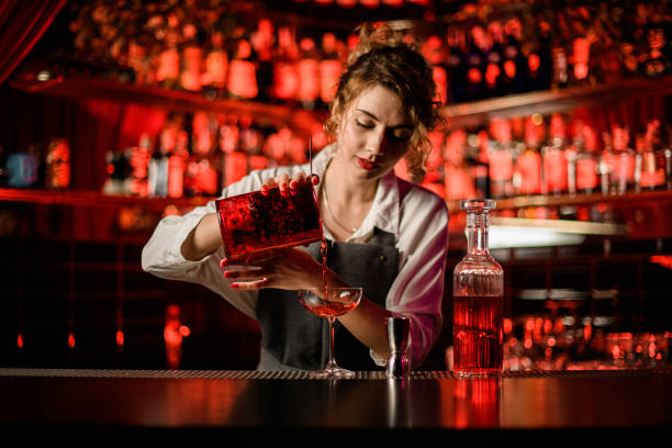 young female bartender pouring bright cocktail into glass on bar counter