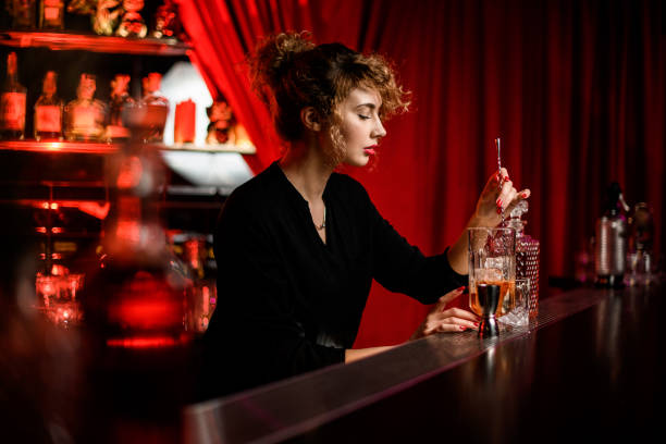 вид на красивую женщину в баре, которая перемешивает коктейль в стакане с ложкой - gin decanter whisky bottle стоковые фото и изображения
