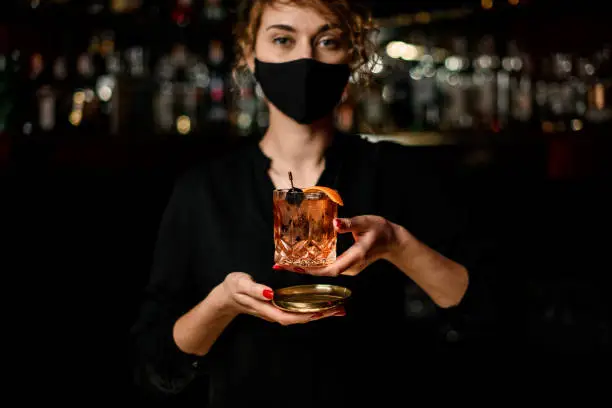 Photo of Close-up view of woman in black mask and holding glass with cocktail